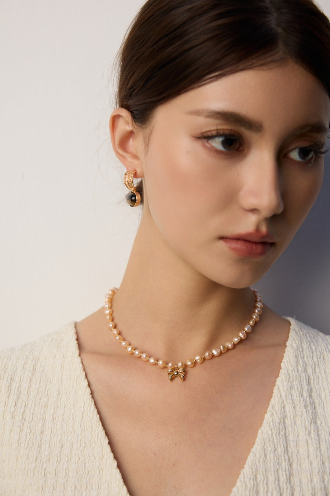 Dark stone drop earring worn beside a pale textured V-neck