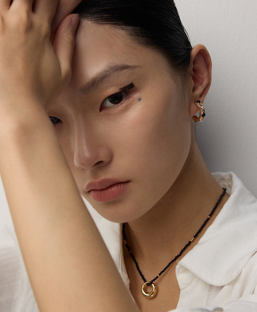 Minimal black agate necklace and warm gold-tone earrings in a close portrait