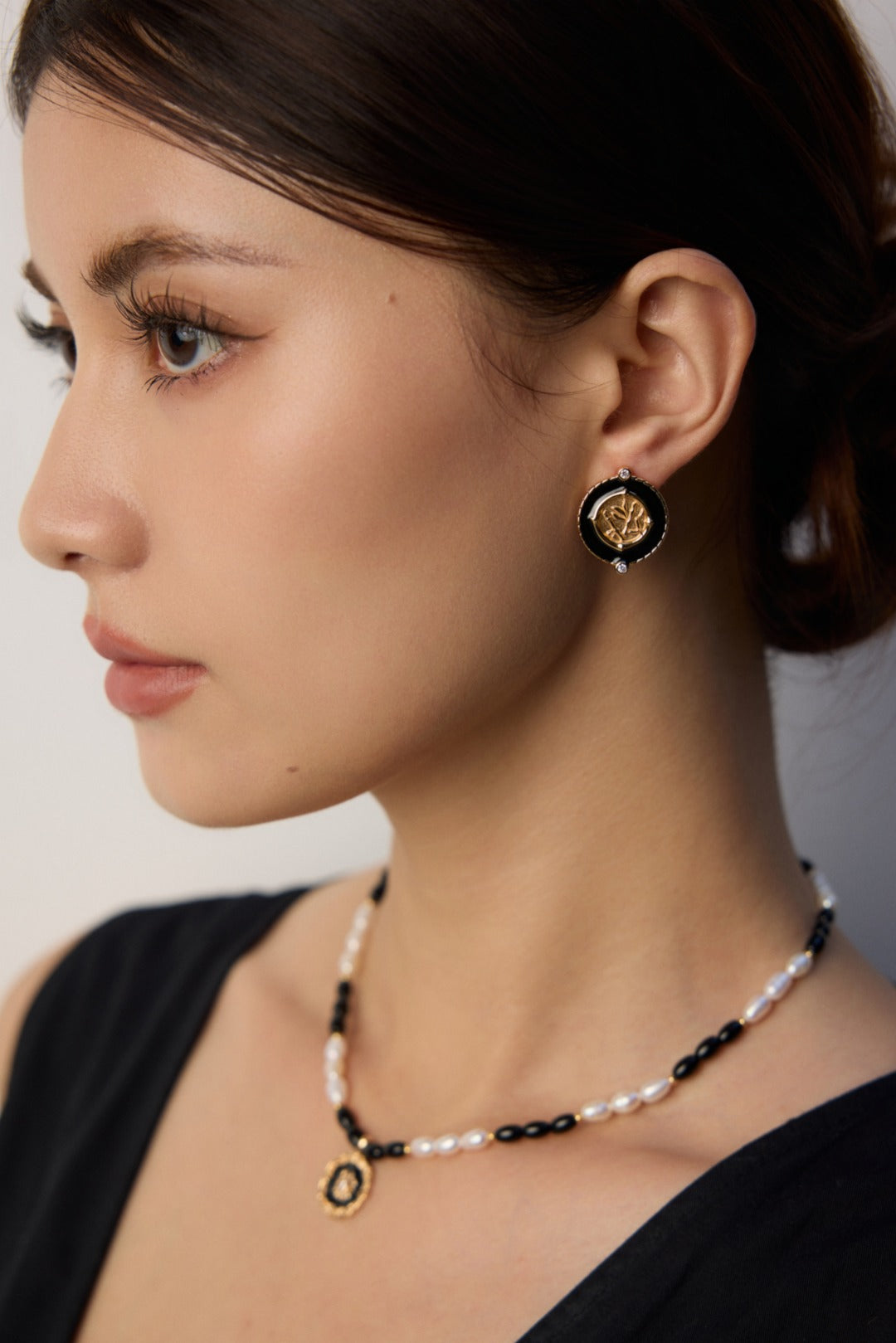 Black enamel round earring worn beside an open black neckline