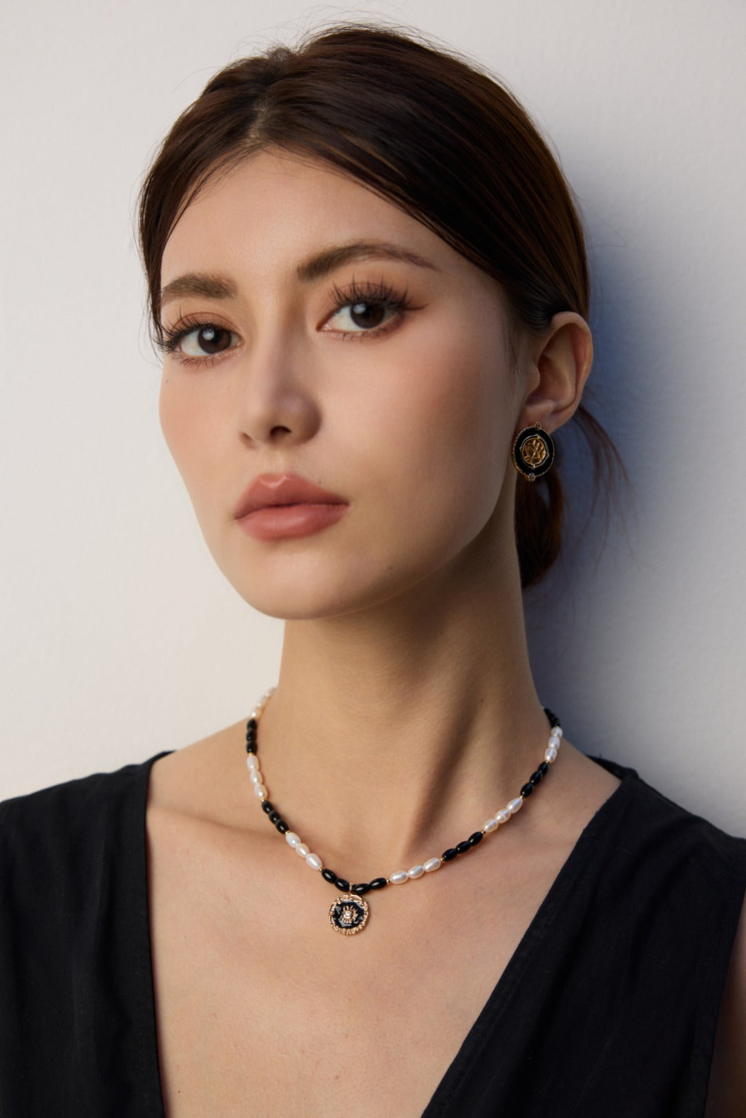 Black enamel round earring worn beside a deep black V-neck
