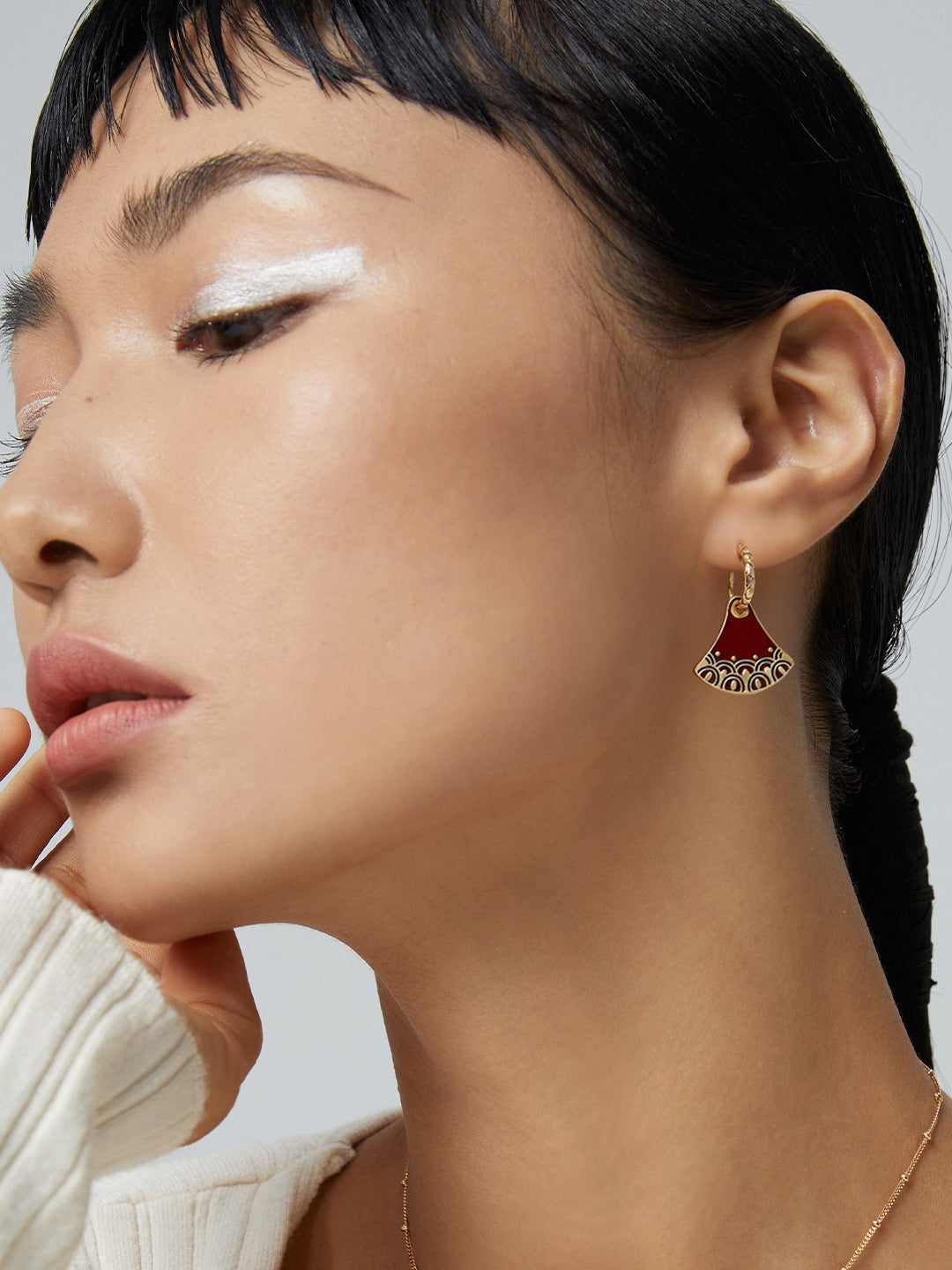 Red enamel drop earring shown with dark hair drawn back from the ear